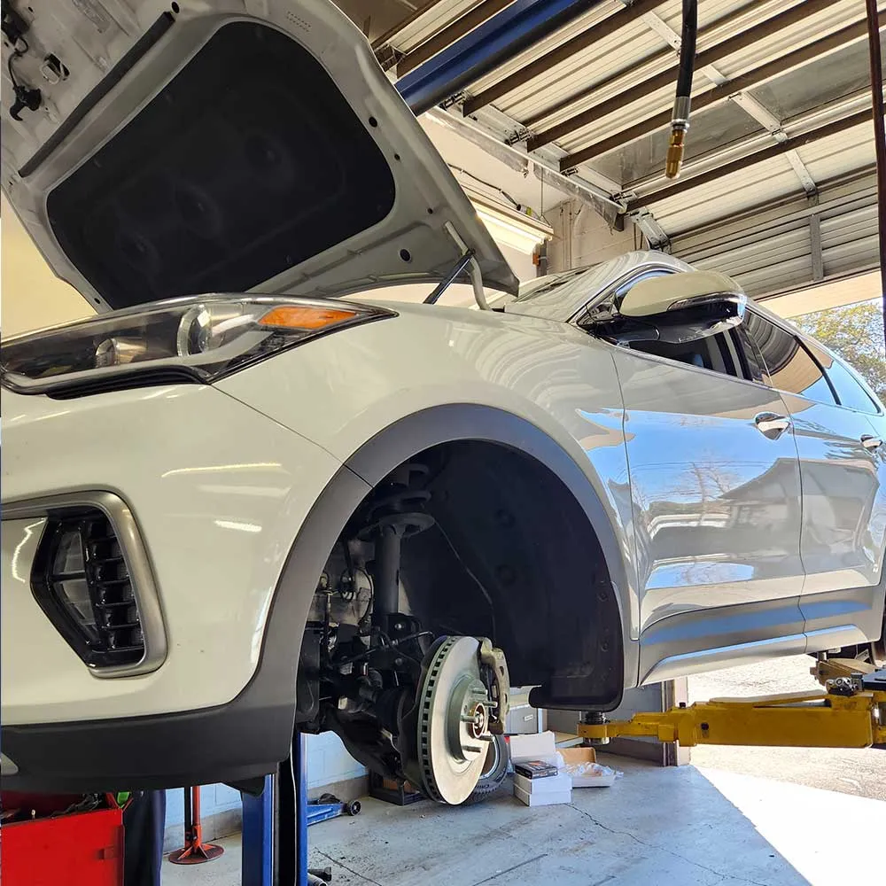 Car on lift undergoing brake maintenance in garage.