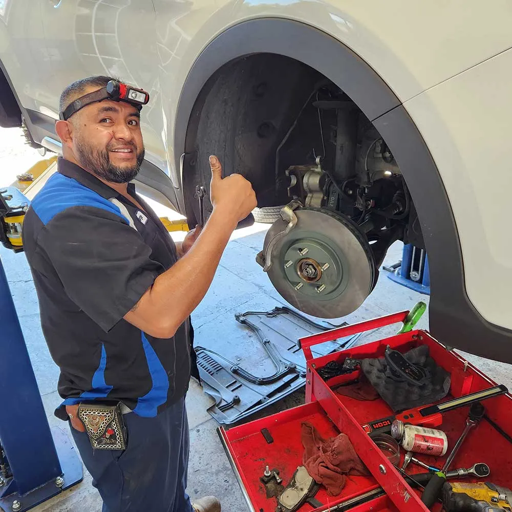 Mechanic giving thumbs up during car brake repair.